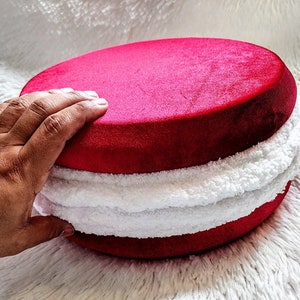 May include: A red velvet cushion with a white fluffy trim. The cushion is round and has a soft, plush texture.