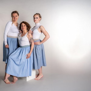 May include: Three people wearing matching outfits. Each person is wearing a white top and a light blue skirt. The skirts have a decorative band at the waist. The outfits are suitable for a dance or performance.