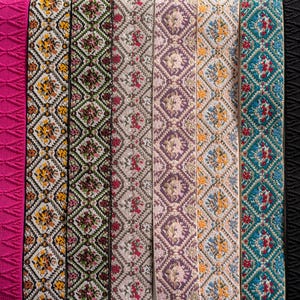 May include: A collection of decorative ribbons in various colors and patterns. The ribbons include a light green diamond pattern, a bright pink textured design, and several floral and geometric patterns in shades of yellow, red, and purple. Other ribbons are black and tan.