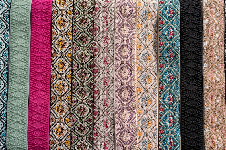 May include: A collection of decorative ribbons in various colors and patterns. The ribbons include a light green diamond pattern, a bright pink textured design, and several floral and geometric patterns in shades of yellow, red, and purple. Other ribbons are black and tan.