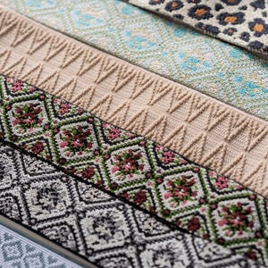 May include: Close-up of various patterned ribbons. Designs include floral, geometric, and animal print patterns. Colors include beige, green, black, white, and blue. The ribbons are likely used for crafting or sewing projects.