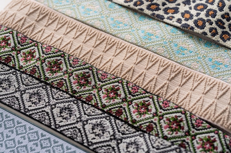 May include: Close-up of various patterned ribbons. Designs include floral, geometric, and animal print patterns. Colors include beige, green, black, white, and blue. The ribbons are likely used for crafting or sewing projects.