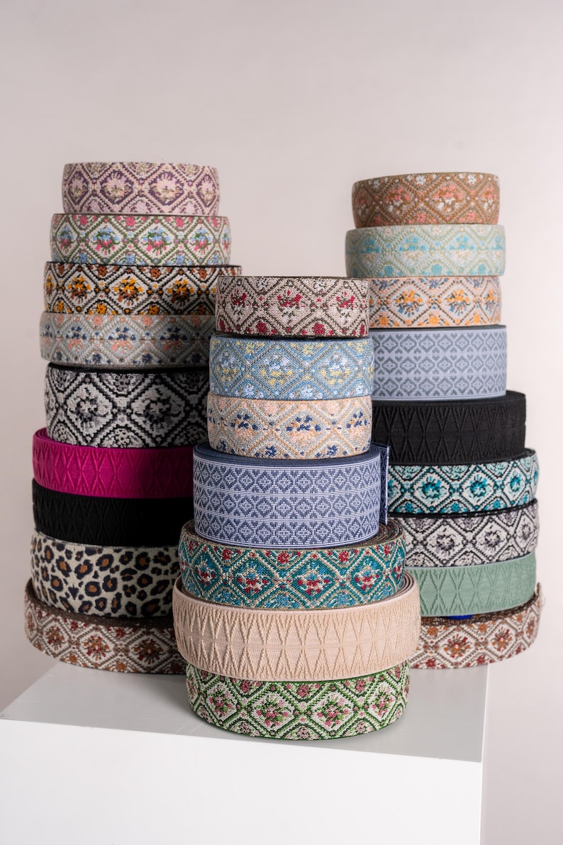 May include: A collection of decorative ribbons in various colors and patterns. The ribbons are stacked in rolls, showcasing floral, geometric, and animal print designs. Colors include pink, black, beige, and teal. The ribbons are suitable for crafts and embellishments.