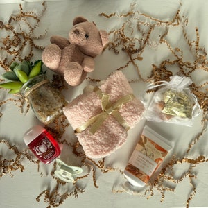 May include: A gift basket with a pink fuzzy blanket, a small teddy bear, a bottle of hand cream, a small bottle of hand sanitizer, and a small bag of chocolate candies.