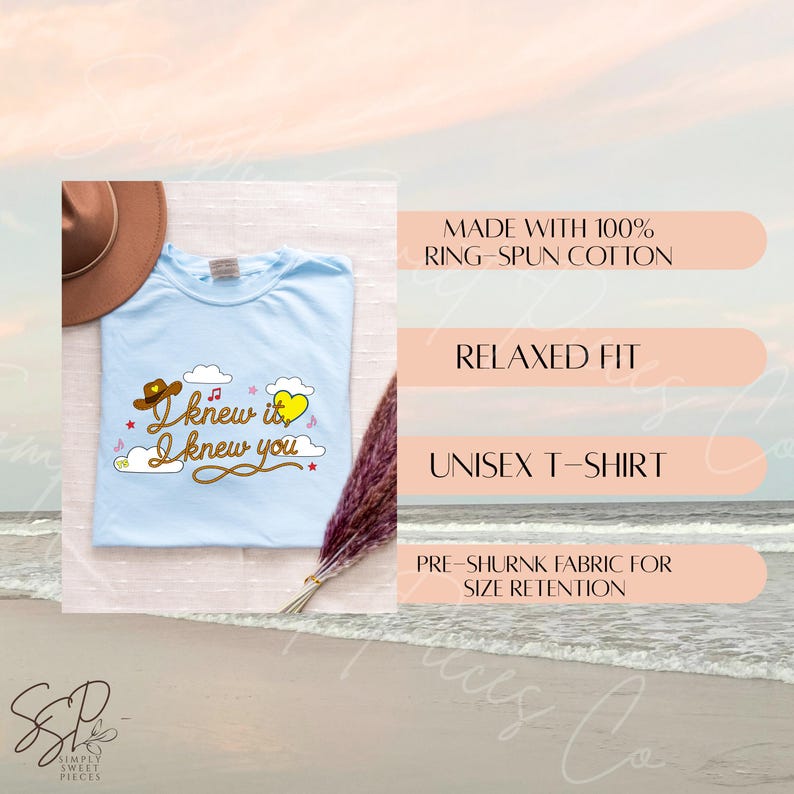 May include: A light blue t-shirt featuring a brown cowboy hat, a yellow heart, white clouds, and the text "I knew it I knew you" in a cursive font. The shirt is displayed with a brown hat and a dried floral stem, with text listing product details.