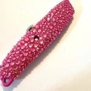 May include: A pink utility knife with a handle covered in pink rhinestones.