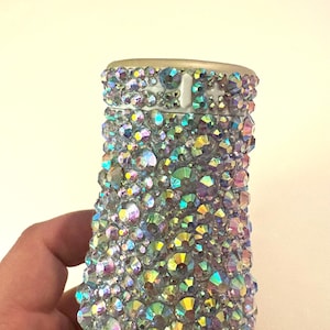 Puede incluir: Una funda de teléfono blanca cubierta de piedras de cristal iridiscentes.