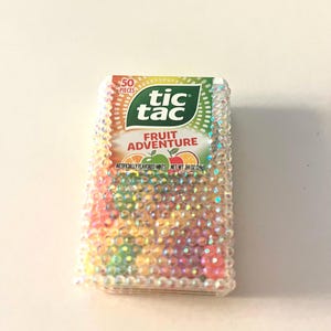 May include: A bedazzled Tic Tac box with the words "Fruit Adventure" and "50 Pieces" visible. The box is covered in iridescent rhinestones, with a green and white Tic Tac logo. The mints are artificially flavored and weigh 0.34 oz.