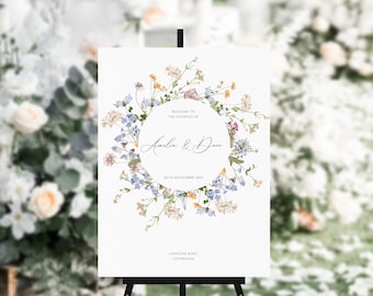 May include: A white wedding welcome sign with a floral wreath design in shades of blue, yellow, and pink. The text reads "Welcome to the wedding of Amelia & Dave, 20th September 2021, Lapstone Barn, Chichester".