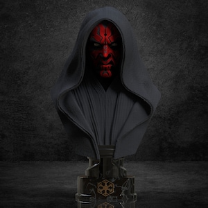 Könnte beinhalten: Eine schwarze und rote Büste von Darth Maul, einem Charakter aus dem Star Wars-Franchise. Die Büste trägt eine schwarze Kapuzenrobe und hat ein rotes Gesicht mit schwarzen Markierungen. Die Büste steht auf einem schwarzen Marmorsockel mit einem goldenen Symbol.