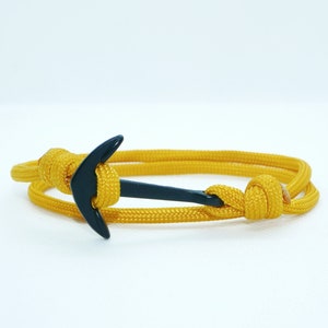 Könnte beinhalten: Ein gelbes Paracord-Armband mit einem schwarzen Anker-Anhänger.