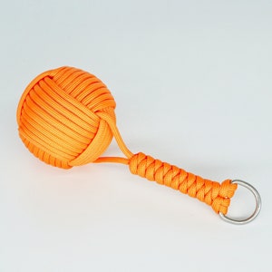Op de afbeelding: Oranje paracord sleutelhanger met een geknoopte bal aan het einde en een zilveren sleutelring.