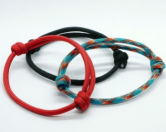 May include: Three braided rope bracelets in red, black, and blue with a multi-colored pattern. The bracelets are tied in knots.