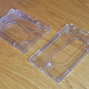 K&ouml;nnte beinhalten: Zwei transparente Plastik-Ausweishalter. Die Halter sind f&uuml;r die Aufnahme eines standardm&auml;&szlig;igen Personalausweises oder einer Kreditkarte konzipiert.