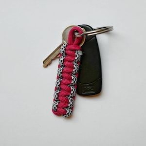 May include: A pink and black paracord key chain with a silver key and a black key fob.