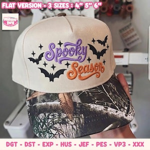 May include: A cream-colored baseball cap featuring an embroidered design with the purple text Spooky and orange text Season, accented by black bats and star shapes. The brim has a camouflage pattern. The text 3 sizes 4 5 6 is visible.