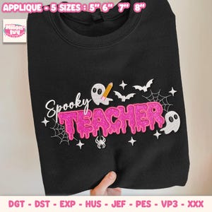 May include: A black sweatshirt featuring an embroidered design with the text Spooky TEACHER in pink glittery letters. The design includes white ghosts, a yellow pencil, spider webs, a spider, and small stars. Available in 5 sizes: 5, 6, 7, and 8 inches.