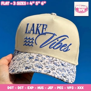Könnte beinhalten: Beige Baseball Cap mit den blau gestickten Worten "LAKE Vibes". Der Schirm hat ein Blumenmuster mit blauen Blumen. Erhältlich in den Größen 10, 12.7 und 15.2 cm.