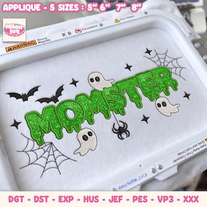 May include: An embroidery design in a white hoop featuring the green glittery text "MOMSTER" in a dripping font. The design includes three white ghosts, two black bats, two spider webs, a black spider, and several small black four-pointed stars.