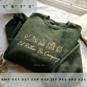 May include: A dark green sweatshirt with the text "I'd Rather Be Camping" in a gold color. The design includes a tent, campfire, backpack, and lantern. The sweatshirt is shown with a measuring guide of 5 to 8 inches.
