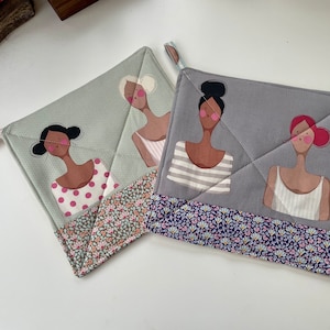 May include: Two green and grey quilted pot holders with floral trim. Each pot holder features a different illustration of a woman with a different hairstyle and outfit.