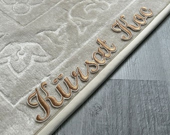 May include: A white plush rug with a gold embroidered border. The border features the text "Kürsat Hac".