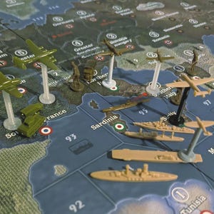 May include: A strategic board game with miniature military units. The game board depicts a map with countries and territories. The image shows miniature airplanes, tanks, and ships in various positions, suggesting a war game scenario.