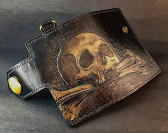 May include: A black leather wallet with a tooled design of a skull and crossbones. The skull is gold and the crossbones are brown.