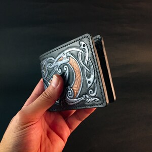May include: Black leather wallet with a silver and brown Celtic knot design.