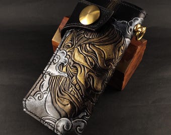 May include: A black leather wallet with a gold and silver embossed design of a Japanese demon. The wallet has a brass button closure and a chain attached to the side.