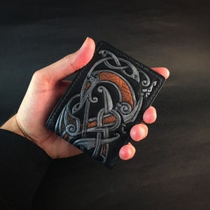 May include: Black leather wallet with a silver and orange embossed design of a mythical creature.
