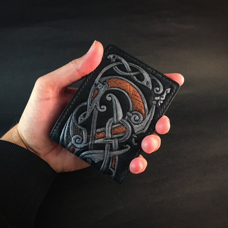 May include: Black leather wallet with a silver and orange embossed design of a mythical creature.