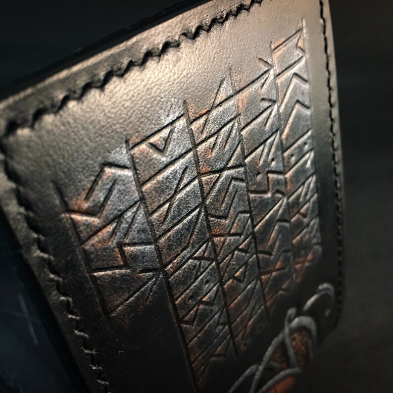 May include: A black leather wallet with a geometric pattern embossed in silver and copper.