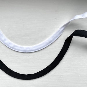 May include: Two fabric trim pieces, one white and one black, with white plastic ends. The trim pieces are curved and are lying on a white surface.