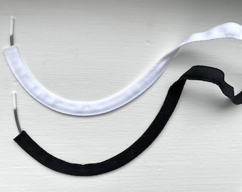 May include: Two fabric trim pieces, one white and one black, with white plastic ends. The trim pieces are curved and are lying on a white surface.