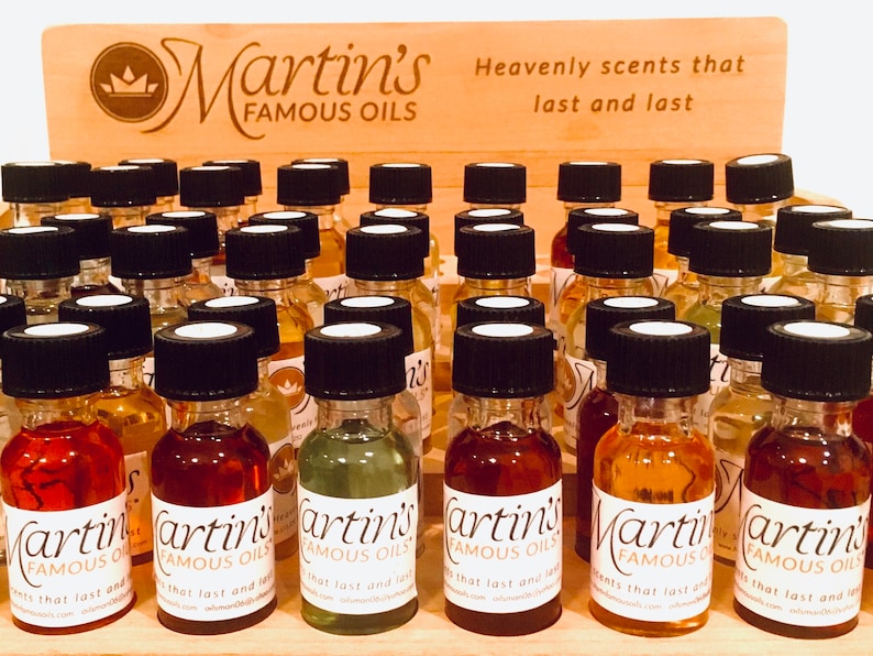 Op de afbeelding: Een houten display gevuld met kleine glazen flesjes met etherische oli&euml;n. De flesjes hebben zwarte dopjes en witte etiketten met de tekst "Martin's Famous Oils". Het display heeft een bord met de tekst "Heavenly scents that last and last".