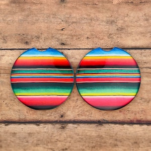 May include: Two round, colorful, patterned coasters with a cut-out for a beverage. The coasters feature a red, yellow, green, blue, and black striped pattern.