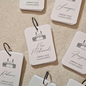 May include: A set of white Umrah Dua flashcards with a black outline of the Kaaba and the text "Umrah Dua Flashcards" on each card. The cards are organised in a stack and have a black ring binder.