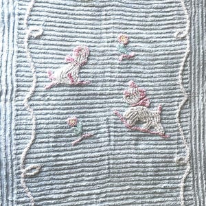 May include: Light blue textured fabric with a repeating pattern of embroidered figures. The figures are white with pink accents, and the border is a white, looped design. The overall theme is whimsical and decorative.