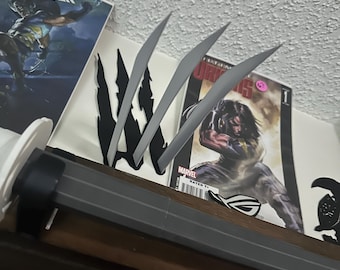 May include: A display featuring comic books and a replica of Wolverine's claws. The claws are silver and sharp, positioned above a dark gray handle. Comic books include the X-Men and Marvel series.
