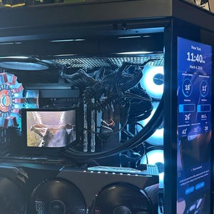 Puede incluir: Una carcasa de ordenador personalizada con componentes internos visibles. La carcasa negra tiene una pantalla digital que muestra la hora y la temperatura. Cuenta con ventiladores iluminados, sistemas de refrigeración y una figura decorativa alienígena.