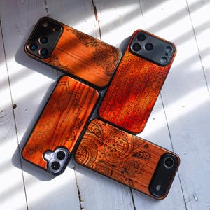 Könnte beinhalten: Vier Handyhüllen aus Holz mit aufwendigen, lasergeschnittenen Designs. Die Hüllen haben eine warme, rötlich-braune Farbe mit detaillierten Mustern. Sie liegen auf einer weißen Holzoberfläche, mit Schatten.