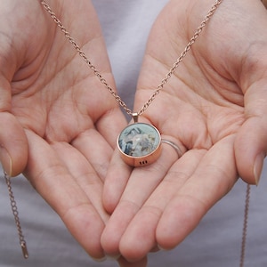 Op de afbeelding: Een ketting van roségoud met een ronde hanger met een blauw en wit beeld erin. De hanger heeft een gladde, metalen afwerking.