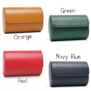 May include: Four cylindrical watch cases with a smooth finish and a flap closure. The colors are orange, green, red, and navy blue. Each case is labeled with its respective color name in black text: Orange, Green, Red, and Navy Blue.