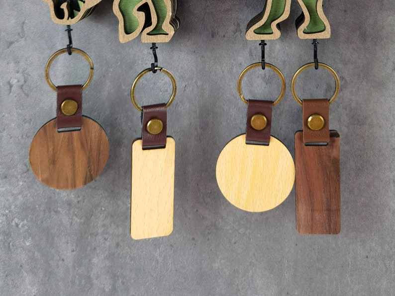 May include: Four wooden keychains with leather straps and metal rings. Two keychains are round, one is light brown and one is dark brown. The other two keychains are rectangular, one is light brown and one is dark brown.