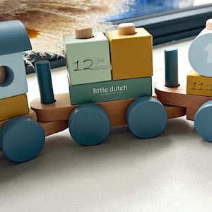 May include: A blue and yellow wooden toy train with a personalised name tag that says "Jamie". The train has a number block that says "12 Jul 2020" and another block that says "little dutch".