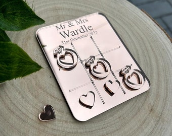 Könnte beinhalten: Rosenvergoldetes Spiegelspielbrett mit dem Text "Mr & Mrs Wardle 31st December 2022" und herzförmigen Ausschnitten. Das Brett liegt auf einer Holzoberfläche.