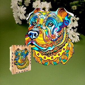 Puede incluir: Un colorido rompecabezas de madera y una caja de madera con la cara de un perro. El dise&ntilde;o utiliza tonos de azul, amarillo, naranja y verde, creando un efecto visual llamativo. La cara del perro es el foco central de la obra.