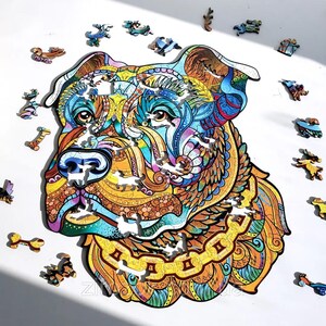 Puede incluir: Un colorido rompecabezas de madera con la imagen de la cabeza de un perro con intrincados patrones en tonos azules, amarillos, naranjas y marrones. Varias piezas peque&ntilde;as y &uacute;nicas del rompecabezas est&aacute;n dispersas.