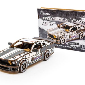 Op de afbeelding: Een 162-delige 3D-houten modelkit van een muscle car met een zebraprint. De doos toont een zwart-witte afbeelding van de auto met de tekst "Muscle Car GT" en "ECO".